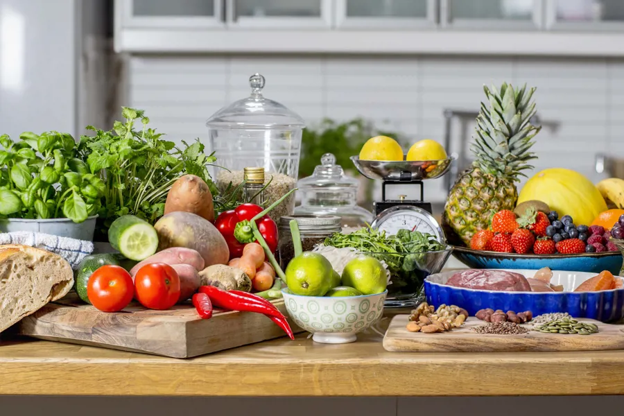 Kjøkkenbenk med ulike matvarer&#58; brød, grønnsaker, nøtter, frukt og urter. Foto