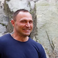 En mann som smiler foran en steinvegg