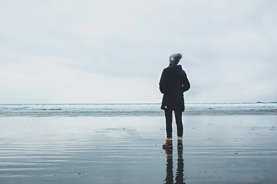 Foto av en godt kledd person som står på en våt strand og ser ut over havet