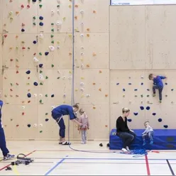 Barn og voksne i en gymsal med klatrevegg