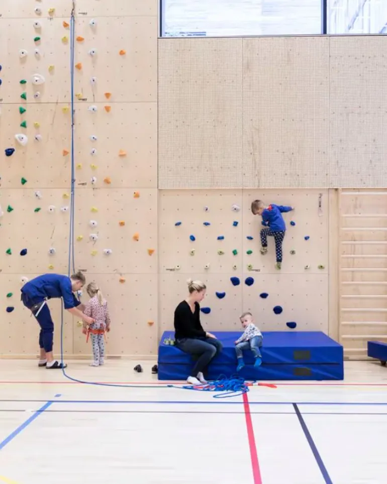Barn og voksne i en gymsal med klatrevegg