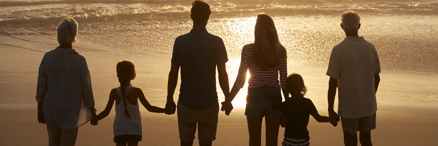 Flere generasjoner som holder hender på en strand i solnedgang