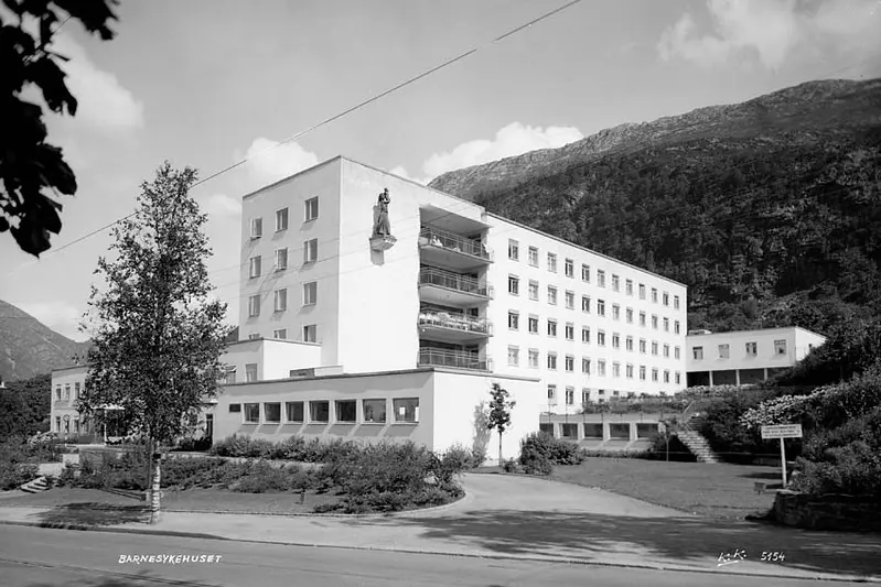 Sort hvitt foto av den gamle barneklinikken med statue hengende på veggen