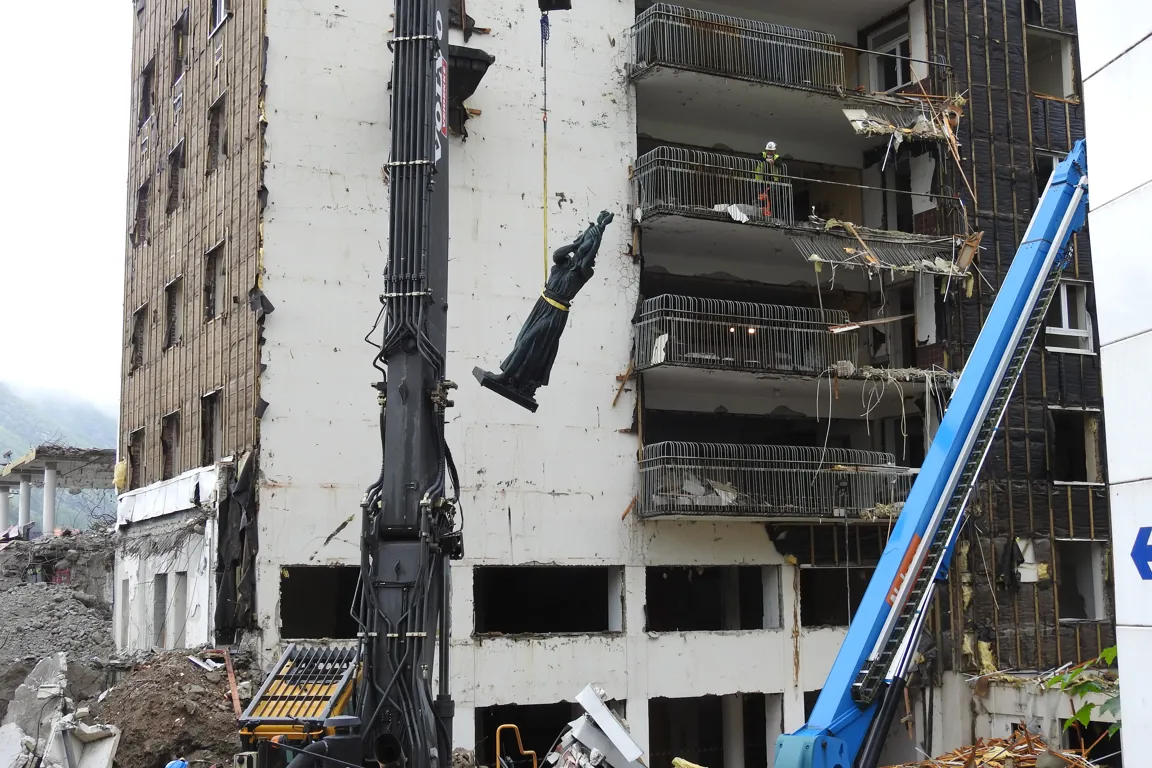 En bygning som rives og en statue heises ned med kran