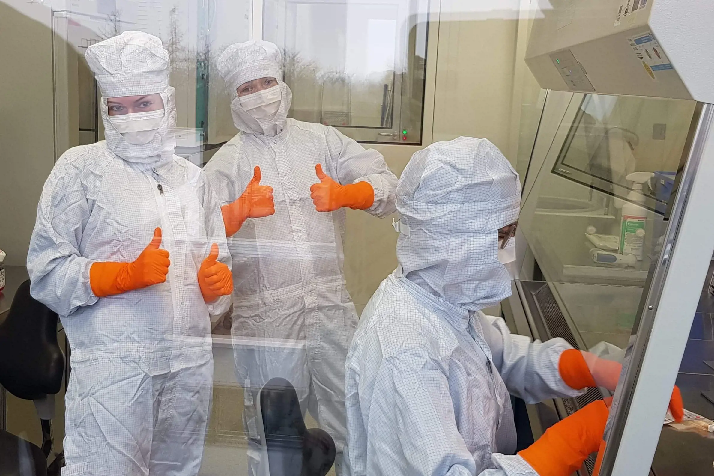 Three persons dressed in infection control equipment in clean room. Photo