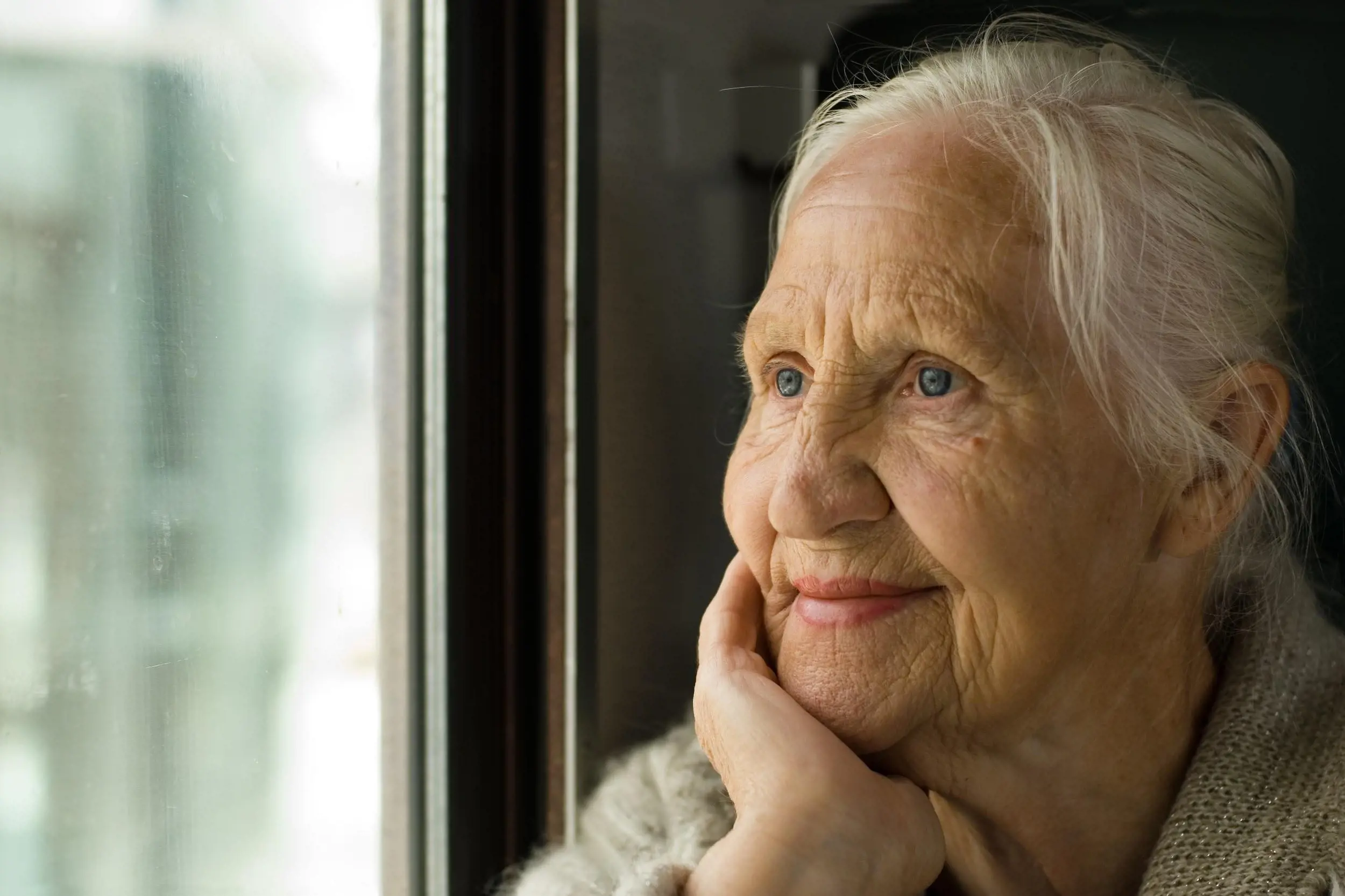 Ei eldre, oppvakt robust kvinne titter ut eit vindu. Foto: Colourbox.  