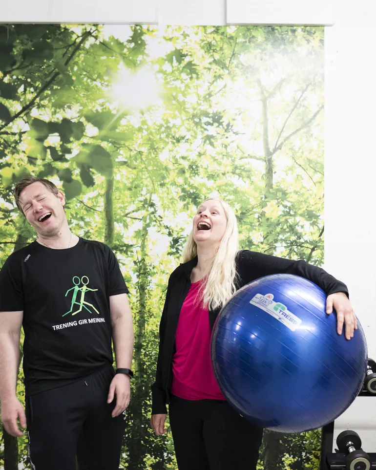 En mann og kvinne ler, kvinne holder stor blå treningsball. Foto
