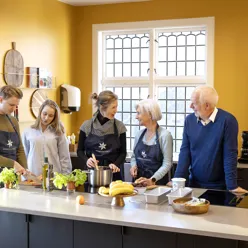 To menn og tre kvinner bak en kjøkkenbenk, lager mat og prater