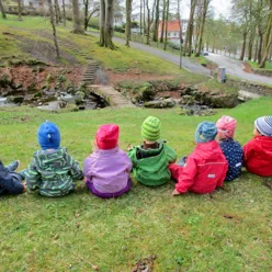 gruppebilde barn sitter på gressplen med ryggen til. Foto