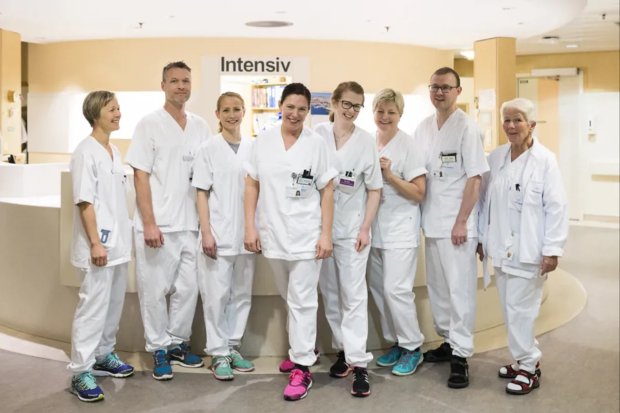 syv sykepleiere som står oppstilt framfor skranken på intensiv og smiler