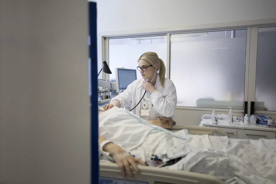 helsepersonell som står å lytter med stetoskop på pasient som ligger i seng