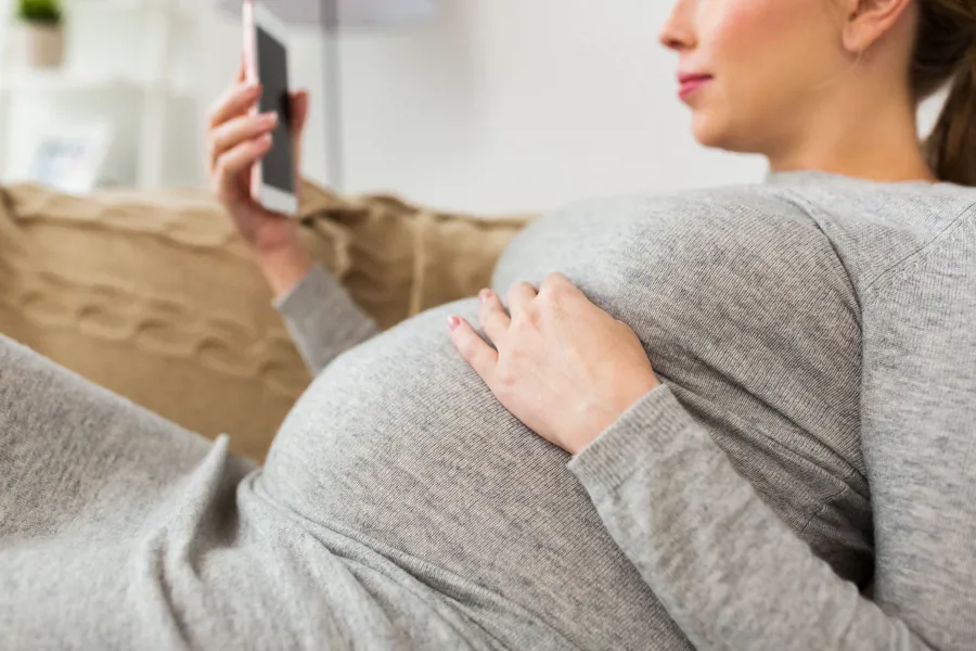 Gravid kvinne med smarttelefon. Foto