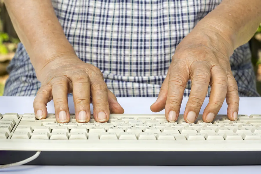 Hendene til eldre mann på tastatur. Foto