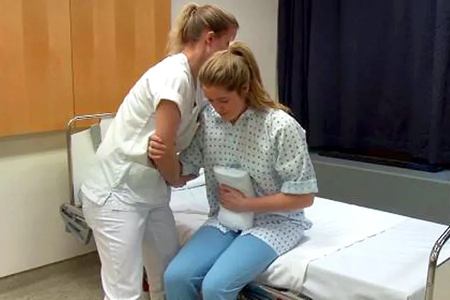 Sykepleier hjelper pasient ut av sengen. Foto