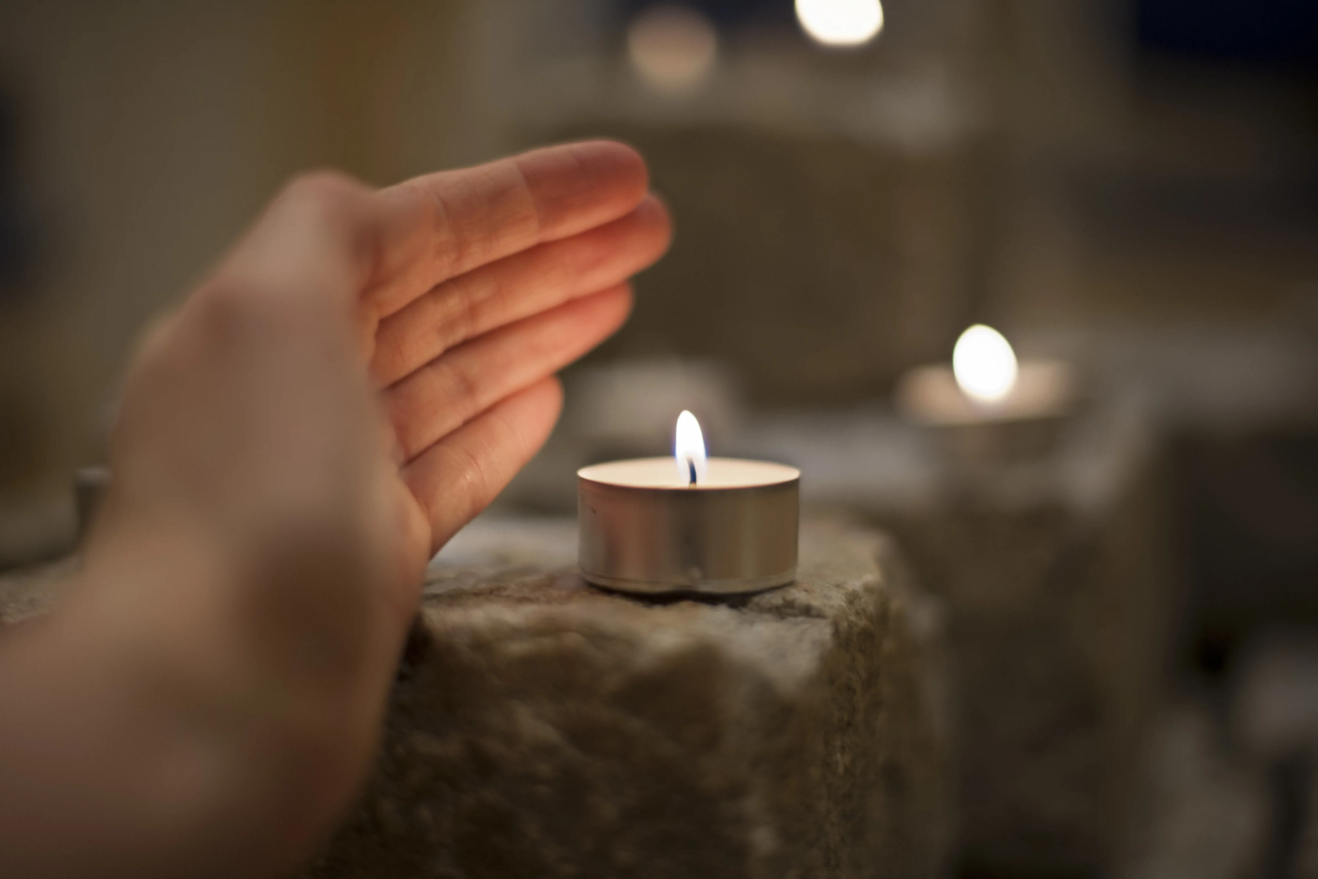 Open hand held close to lit candle on a stone brick. Photo