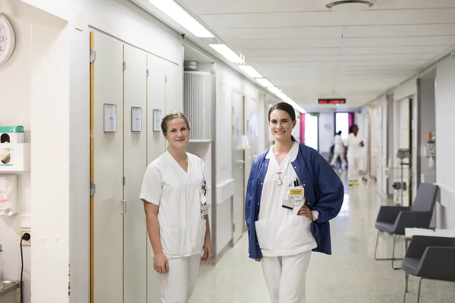 To kvinnelige helsepersonell står i korridor på sengepost. Foto