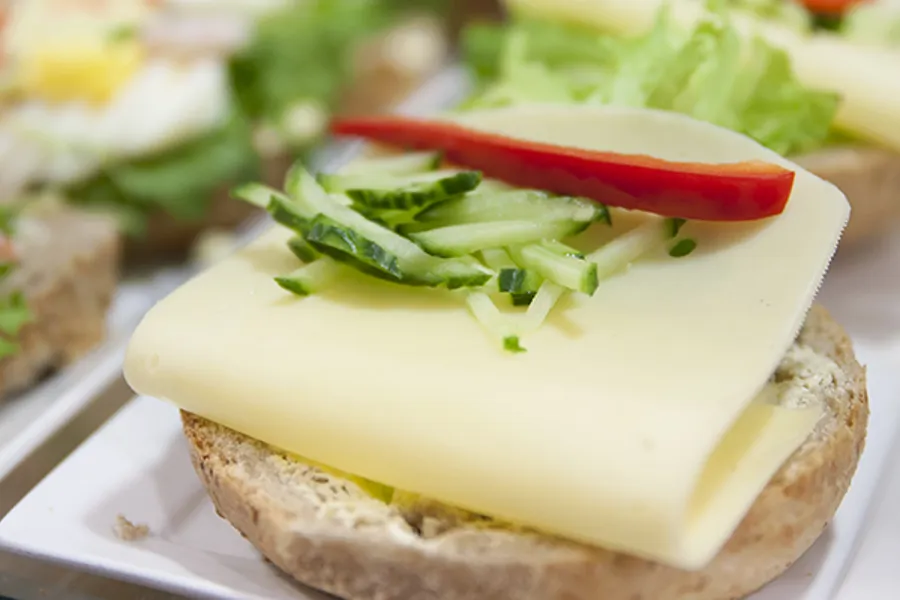 Halvt rundstykke med hvitost, agurk og paprika. Foto