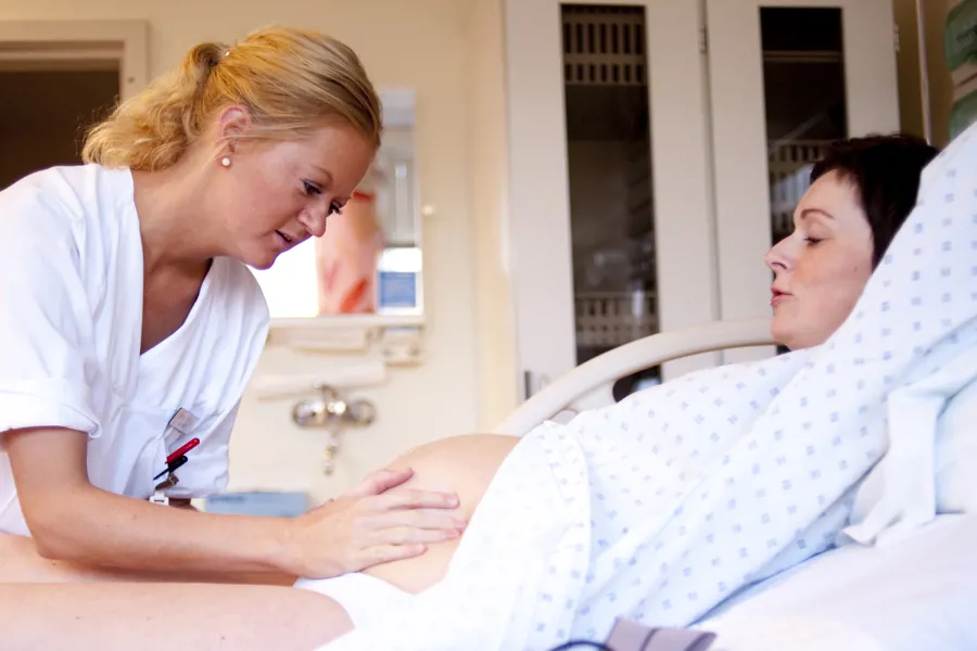 Jordmor undersøker magen til gravid kvinne som ligger i sykehusseng. Foto