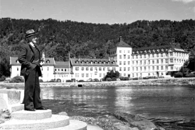 Herman G. Gade står i profil ved vannet med Kysthospitalet i Hagevik i bakgrunnen i 1936. Foto