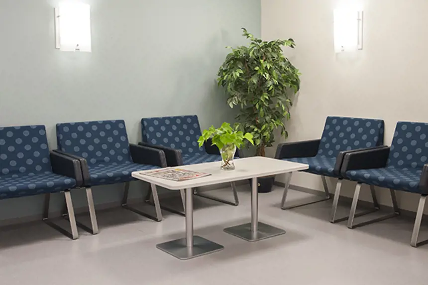Interiør venterom med fem stoler, planter, bord med lesestoff og søppelspann. Foto
