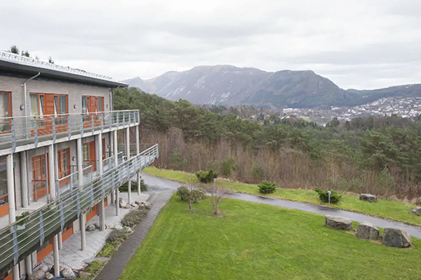 Eksteriør bygg med balkonger og utsikt mot skog, bebyggelse og fjell. Foto