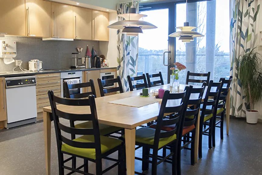 Interiør felles kjøkken med stort spisebord og stoler, kjøkkeninnredning i lyse farger. Foto