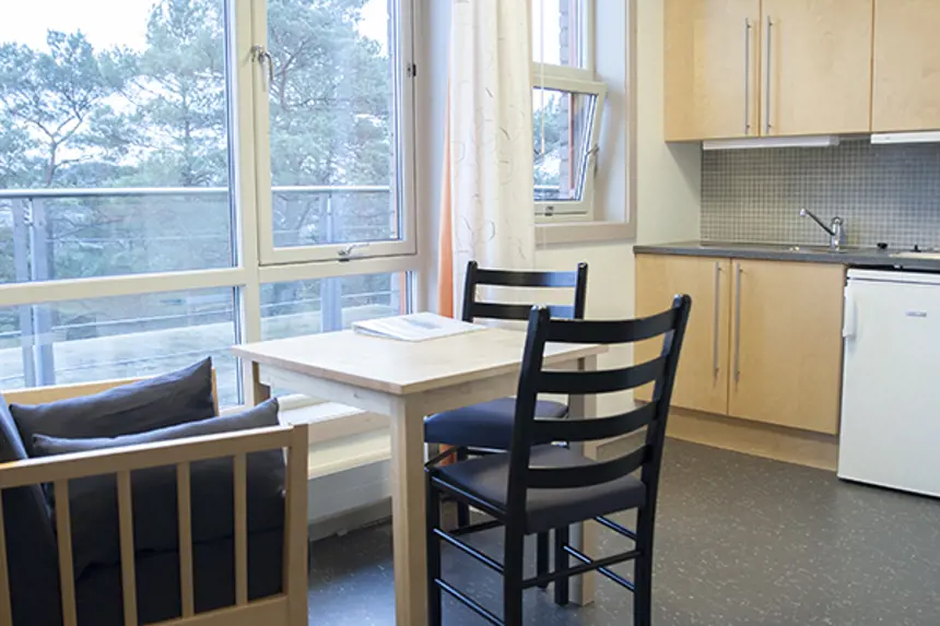 Interiør pasientrom med egen kjøkkenkrok med bord, stoler, kjøleskap, vask, oppvaskmaskin og kjøkkenskap. Foto