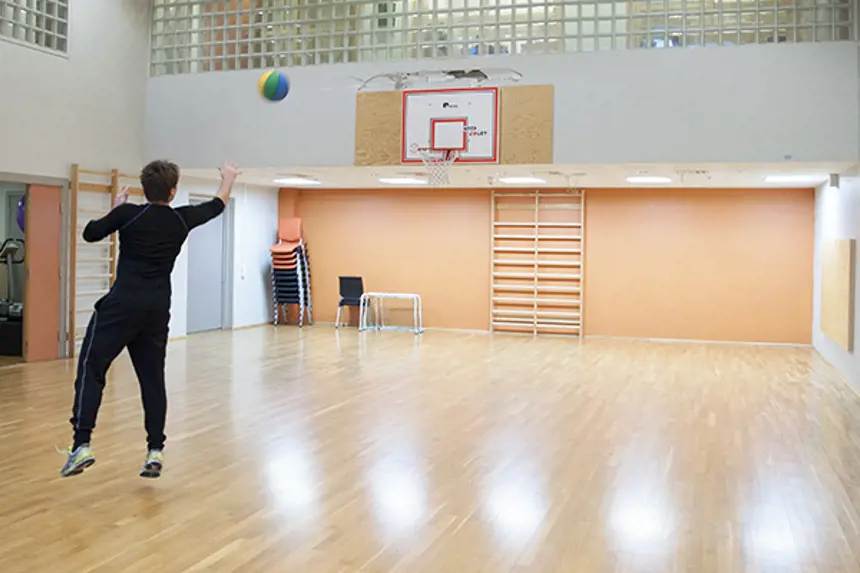 Interiør gymsal, mann som kaster basketball mot basketmål. Foto