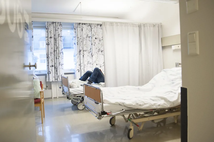Interiør pasientrom på sengepost. To senger med skillegardin mellom, pasient ligger i en av sengene. Foto