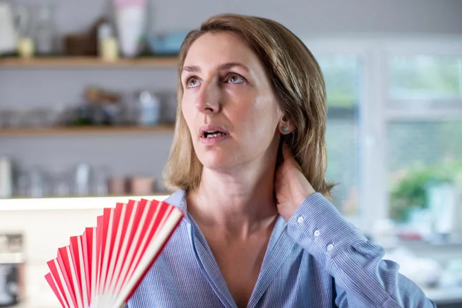 Women with a frustrated look holds her hand to the neck and holding a fan. Photo