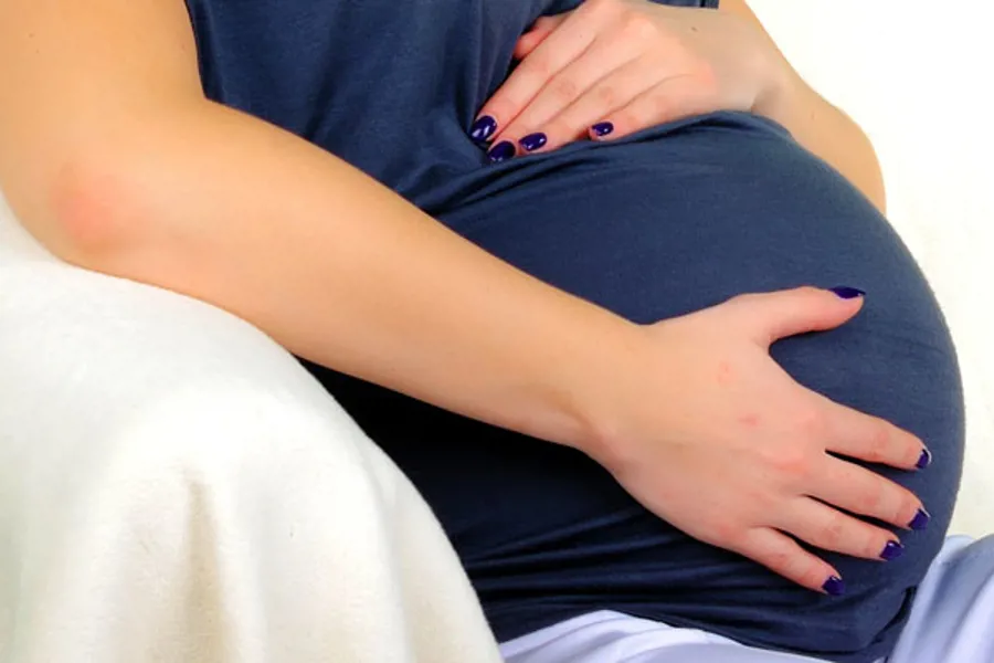 Gravid kvinne holder seg på magen. Foto
