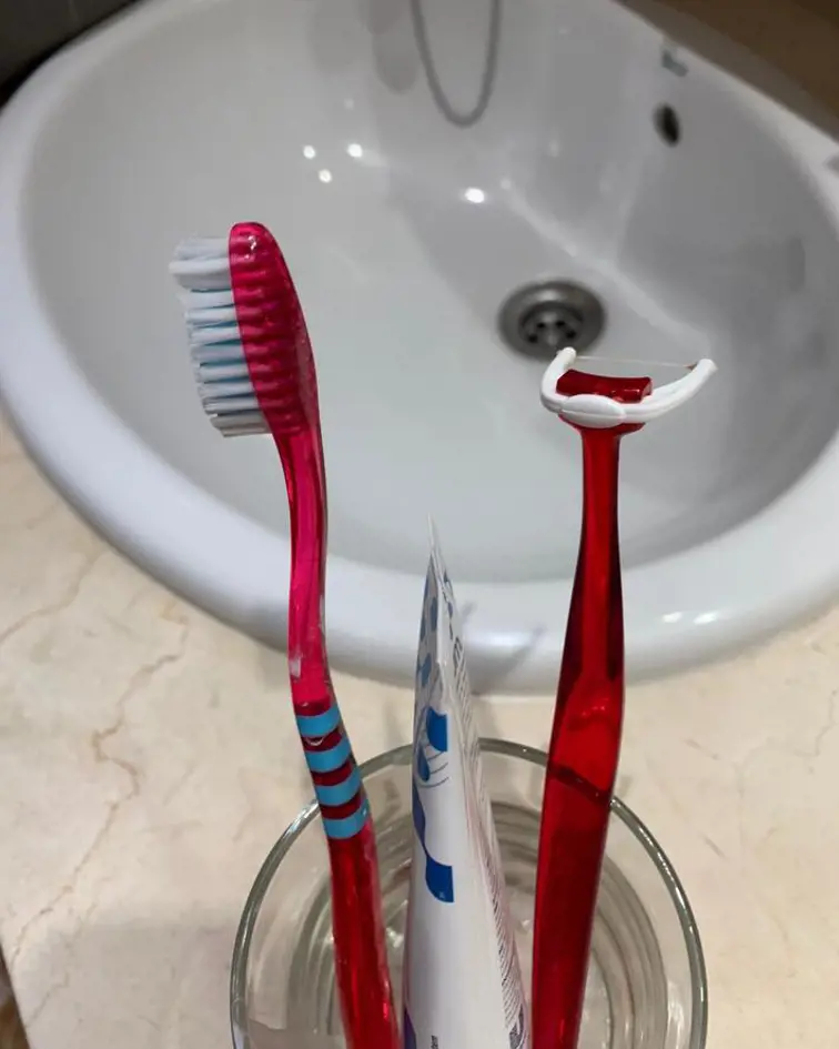 Tannkrem, tannbørste og tanntrådholder i glass ved vaskt / servant. Foto