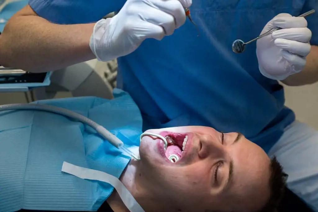 Tannlege og pasient i stolen med spyttsuger i munnen. Foto