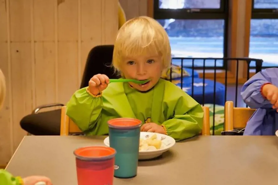 Lyshåret barn som spiser mat i barnehage.