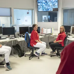 En gruppe mennesker som sitter ved skrivebord i et rom med datamaskiner