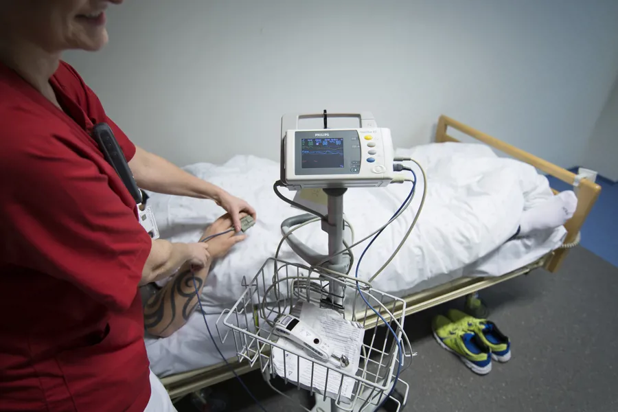 Sykepleier i rød kittel overvåker pasient i seng