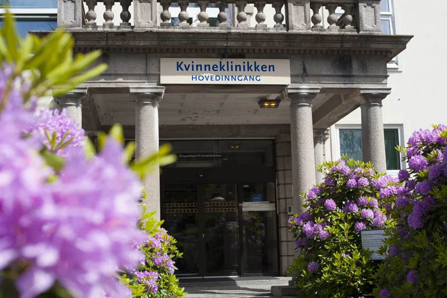 Inngangspartiet på en stor, beige murbygning. Blomster i forgrunnen.